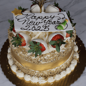 The NY-010 Carrot Cake is a festive treat decorated with strawberries, white chocolate, a gold ribbon, a Happy New Year 2025 sign, and a small champagne bottle on a gold cake board.