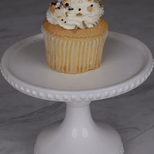 A NY-015 Gold cupcake with chocolate filling and gold sprinkles sits on a white cake stand, topped with a gold 2023 decoration.