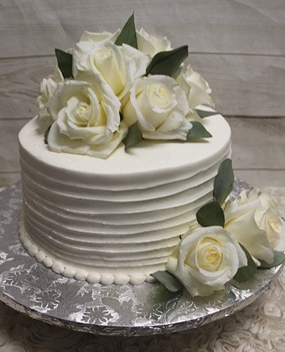 The BR-001 cake features white frosted, textured sides and is adorned with fresh white roses and green leaves, presented on a silver patterned cake board.