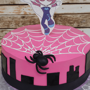 CB-005K is a pink cake with a white icing spiderweb, black fondant spider, black city silhouettes, and a Spider-Gwen superhero pose topper.