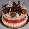 The BD-002B Pina Colada is a round cake topped with chocolate shavings, fresh strawberries, whipped cream swirls, white and dark chocolate décor, toasted coconut flakes, and finished with a red ribbon on a gold cake board.