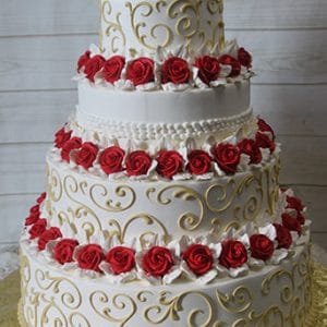 The WC-021 features a four-tier white cake with gold swirl designs and red and white frosting roses on each layer, presented on a gold cake board against a light wood background.