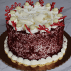 The BD-006C Red Velvet is a round cake with white frosting, topped with white chocolate curls, white chocolate balls, and red chocolate butterfly decorations, presented on a gold cake board.