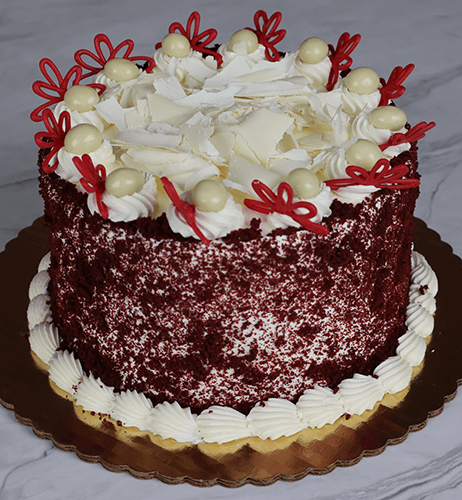The BD-006C Red Velvet is a round cake with white frosting, topped with white chocolate curls, white chocolate balls, and red chocolate butterfly decorations, presented on a gold cake board.