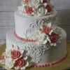 The WC-018 is a two-tiered white wedding cake with intricate swirl designs, topped with white and pink fondant roses clusters, set on a gold cake board.