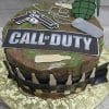 The CB-011S is a round cake featuring a Call of Duty sign, toy handgun, grenade, dog tags, fake bullets, and bottle silhouettes on camo icing with a gold-patterned base.