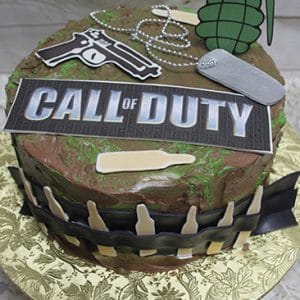 The CB-011S is a round cake featuring a Call of Duty sign, toy handgun, grenade, dog tags, fake bullets, and bottle silhouettes on camo icing with a gold-patterned base.