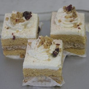 Three AP-045D Pumpkin Square cakes with cream filling, topped with whipped cream, chopped nuts, and dried fruit, are arranged on a silver plate.