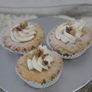 A Pumpkin Cheesecake topped with whipped cream swirls, sprinkled with chopped nuts, and dusted with powdered sugar sits on a reflective silver surface.