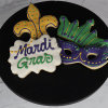 CE-007 Mardi Gras features three decorated cookies on a black plate: a yellow and green fleur-de-lis, a green and purple mask, and a white cookie with “Mardi Gras” in purple and green icing.