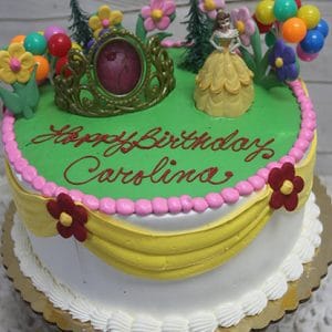 The SC-063 Princess Belle is a round birthday cake with green, pink, and yellow icing, flower decorations, a golden crown, Belle figurine, balloons, and "Happy Birthday Carolina" written in red icing on top.