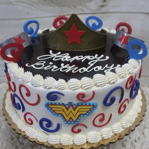 The SC-064 Wonder Woman cake is round, decorated with red, blue, and gold swirls, a Wonder Woman logo and tiara on top, and "Happy Birthday" written in white icing.