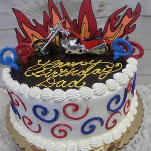 The SC-066 Chopper is a round birthday cake with red and blue swirls, white frosting, a chocolate top, and flame decorations. A toy motorcycle sits on top with “Happy Birthday Dad” written in yellow icing.