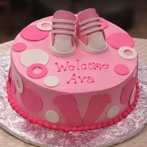 The BB-022 cake is a pink and white baby shower cake decorated with fondant baby shoes, circles, footprints, and “Welcome Ava” written in pink icing.