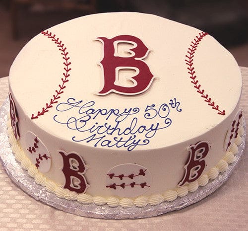 The ST-003 Red Sox cake is round, decorated like a baseball with red stitching and a large red B on top. “Happy 50th Birthday Matty” is written in blue icing, with baseballs and red B’s on the sides.