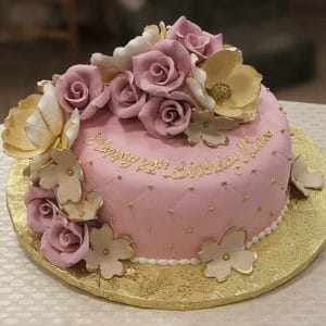 The BR-037 is a round pink birthday cake with gold and white flowers, pink roses, and gold beads. It’s displayed on a gold board with "Happy 21st Birthday Mum" in gold icing.