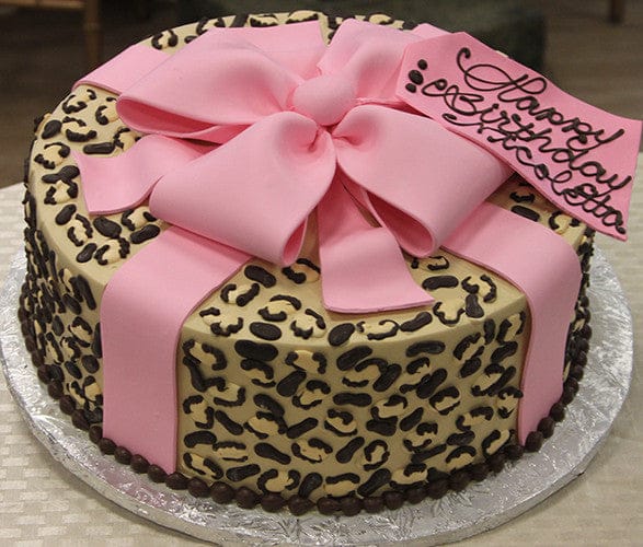 The BD-036B Cheetah Bow Pink is a round cake with a leopard print design, topped with a large pink fondant bow and a pink tag for your birthday message. Presented on a silver board.