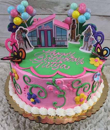 A round SC-030 Barbie cake with pink and green frosting, decorated with butterflies, flowers, balloons, and Barbie & friends toppers. “Happy Birthday Nitya” is written in pink icing.