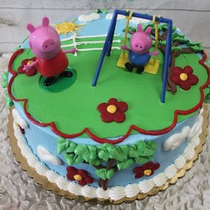 SC-068 Peppa Pig is a round blue cake with clouds, flowers, sun, and piped green grass. Peppa Pig stands on the grass while George sits on a swing. The cake features icing trim and character figurines.