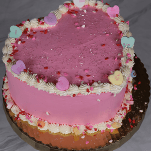 The VC-013D is a heart-shaped pink cake with white frosting along the edges, topped with heart-shaped candies and red, pink, and white sprinkles on a gold cake board.