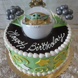 SC-074 Baby Yoda: Round birthday cake with green icing, yellow stars, white swirls, silver balloon clusters, and a Baby Yoda (Grogu) pod topper. "Happy Birthday" is written in white icing.