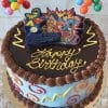 The SC-075 Justice League is a round birthday cake with blue icing, colorful swirls, chocolate frosting, “Happy Birthday” in yellow, Justice League superhero toppers, and candy balloon decorations.