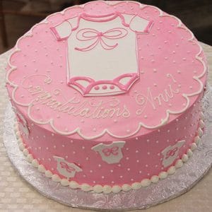 BB-050 is a round pink cake with white polka dots and onesies, topped with a large onesie and the message "Congratulations Anu!", making it perfect for a baby shower celebration.