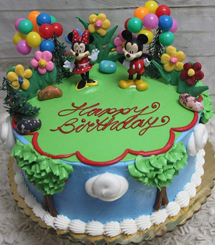 The SC-037 Mickey and Minnie cake features Mickey and Minnie toppers, colorful balloons, flower decor, green icing grass, "Happy Birthday" in red icing, blue sides with tree decorations.