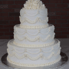 The WC-000C is a three-tiered white wedding cake with elegant piped frosting swags and white icing roses, presented on a silver cake board against a dark brick background.