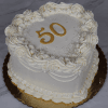 A heart-shaped white cake (BD-023C) with ornate white frosting, silver sprinkles, and a gold "50" topper on a gold board, set against a marble background.