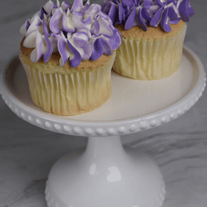 Two CC-019A Gold cupcakes with chocolate mousse filling sit on a white, decorative cake stand against a gray marble background.