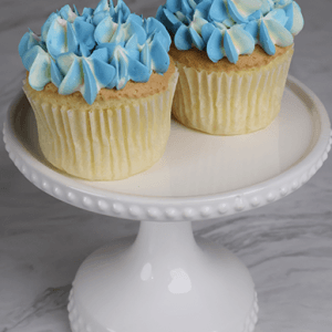 Two CC-017 Gold cupcakes with chocolate mousse filling are displayed on a white, beaded-edge cake stand with a marble background.