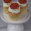 Three CC-098B March Madness Gold Cupcakes with chocolate filling and basketball-themed 2025 toppers sit on a white cake stand. The cupcakes have white frosting, and the background is a light grey marble surface.