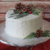 The CH-000D is a white frosted cake adorned with pinecones, cranberries, and green pine branches, presented on a cake stand with a red cloth and wooden background.