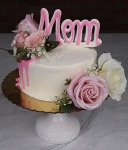 The MD-000C 6"cake petite One Size features white frosting, pink and white roses, baby’s breath, a pink “Mom” topper, gold cake board, white stand, and pink icing dripping down one side.