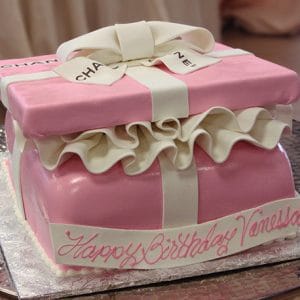 The BD-027F Gift box pink cake is decorated as a pink and white gift box with a bow on top, features ruffled icing, and has “Happy Birthday Vanessa” written in pink icing on the side.