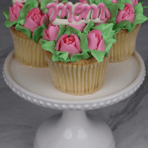 MD-000A Gold cupcakes with chocolate filling, decorated with pink and green icing to resemble flowers, topped with pink "mom" decorations, and displayed on a white cake stand.