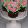 Three MD-000B chocolate cupcakes with white mousse filling, topped with pink mom toppers and rose-shaped frosting, displayed on a white beaded-edge cake stand against a marble background.