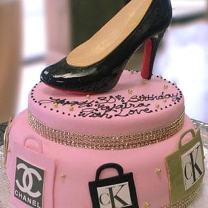 BD-086: A pink two-tier cake with handbag logos, gold ribbon, and a realistic black high-heeled shoe topper, finished with “30th Birthday” in black icing.
