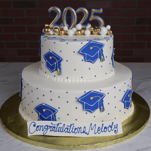 GC-0007 is a two-tiered graduation cake featuring blue graduation caps, gold and white balls, a “2025” topper, and a base plaque with “Congratulations, Melody” in blue icing.