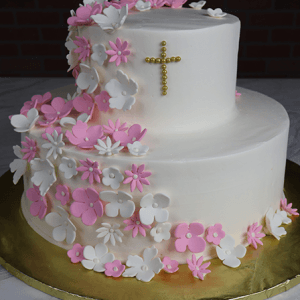 The RC-001E is a two-tier white cake adorned with pink and white fondant flowers and topped with a gold pearl cross, presented on a gold board.