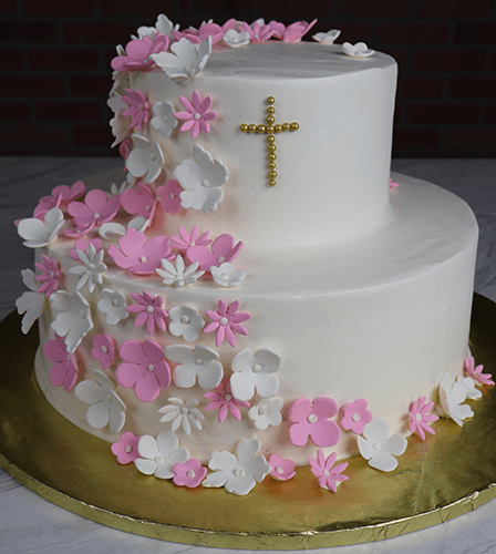The RC-001E is a two-tier white cake adorned with pink and white fondant flowers and topped with a gold pearl cross, presented on a gold board.