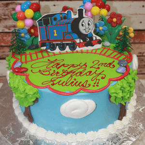 The SC-044 Thomas the Train birthday cake features a Thomas topper, vibrant balloons, flowers, trees, and a red icing track. "Happy 2nd Birthday Julius!!" is written in red icing on the cake.