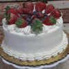 The BD-018M Tres Leches is a round cake covered in white frosting, adorned with whipped cream swirls and topped with fresh strawberries, blueberries, and raspberries, displayed on a gold-rimmed cake board.