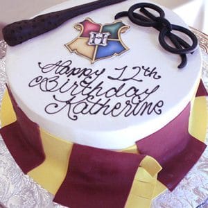 The CB-009Y is a round birthday cake with a Hogwarts crest, magic wand, and black glasses on top. Decorated with maroon and yellow stripes, it features "Happy 12th Birthday Katherine" in script icing.