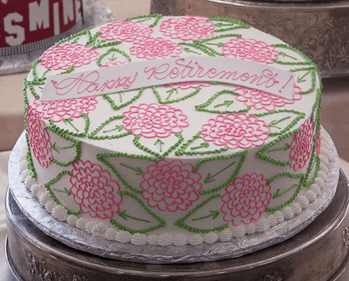 The BD-148 Pink hydrangea is a round white cake with pink flowers and green leaves, topped with a "Happy Retirement!" white banner in pink script, presented on a silver platter.