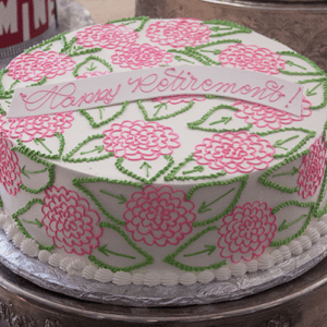 The BR-031 is a round cake with pink and green floral designs, topped with a white banner reading "Happy Retirement!" in pink icing. Presented on a silver tray.
