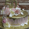 BD-057E Gold Pink champagne frosting cake, round with gold drip, pink and white roses, white flowers, large gold "50" topper, and "Sarah" in gold on the side. Presented on a gold board.