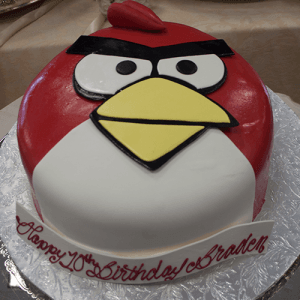 Our CB-011K is a round cake styled as the red Angry Bird with fondant, a yellow beak, and black eyebrows. It sits on a silver base with "Happy 10th Birthday Braden" piped in red icing.