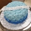 The BD-062 Blue rosette is a round cake with two shades of blue rosette frosting, topped with a white "Happy 1st Birthday Yaim" strip, and displayed on a silver-patterned cake board.